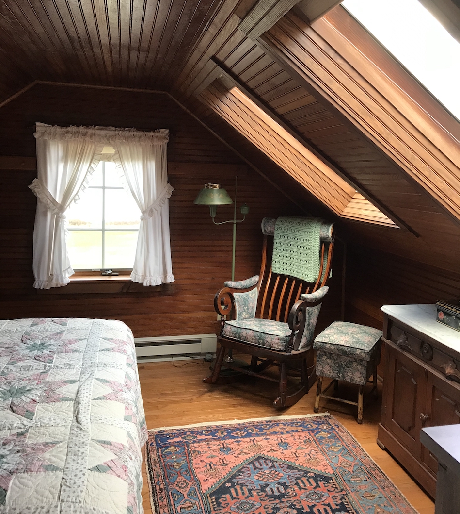 Interior upstairs in a cabin with patchwork quilt on the bed, a rocking chair, rug and windows